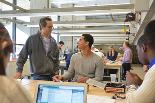 One person standing talking to another person sitting